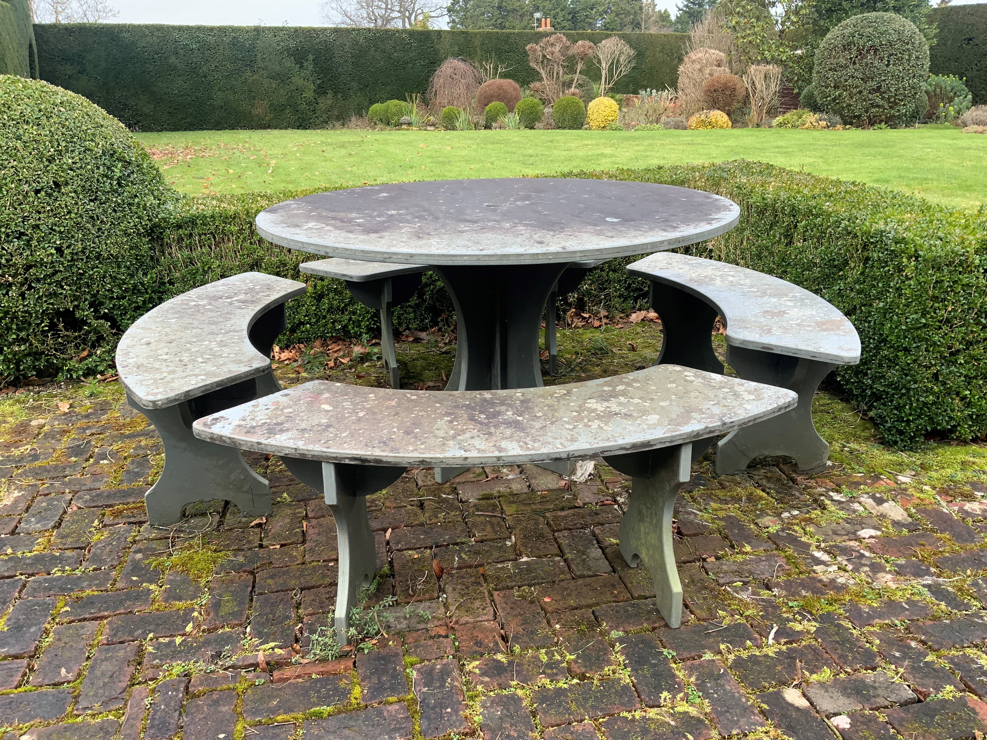 A heavy slate circular topped garden table, diameter 125cm, height 79cm together with four crescent shaped slate garden benches